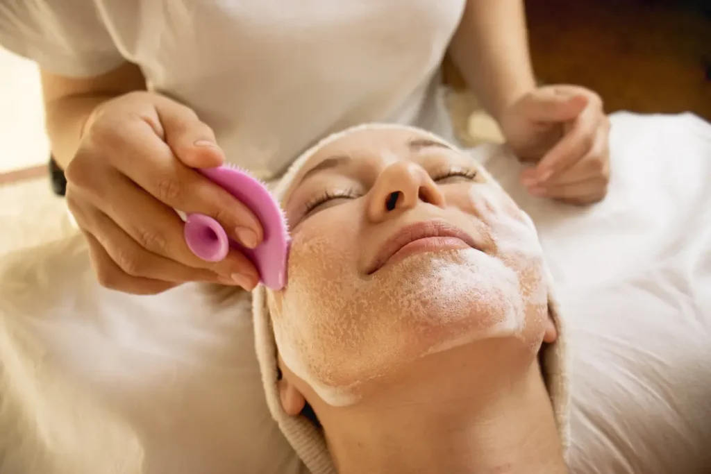 Dermatóloga especialista aplicando un peeling químico suave para potenciar los beneficios de la limpieza facial en el rostro de una mujer.